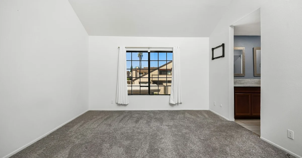 Empty carpeted room with white walls, a large window, and an adjoining vanity area.