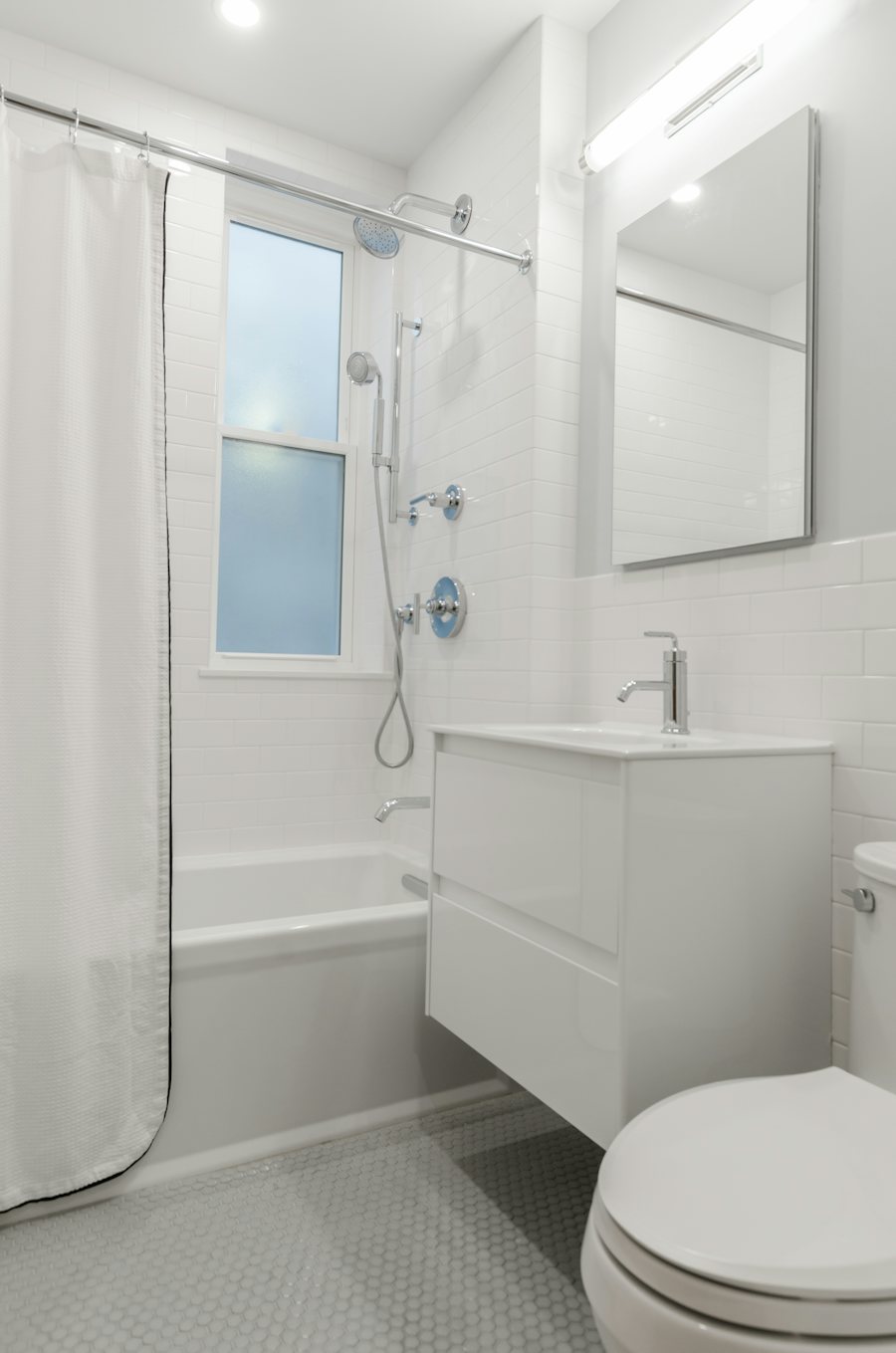 Tub with shower curtain and handheld shower beside a white vanity and toilet.