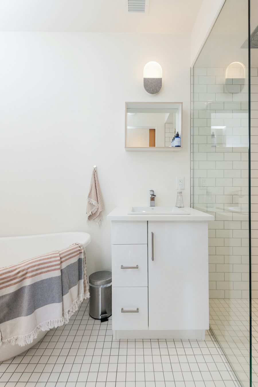 White bathroom vanity with a mirror cabinet, tiled floor, and a glass shower panel.