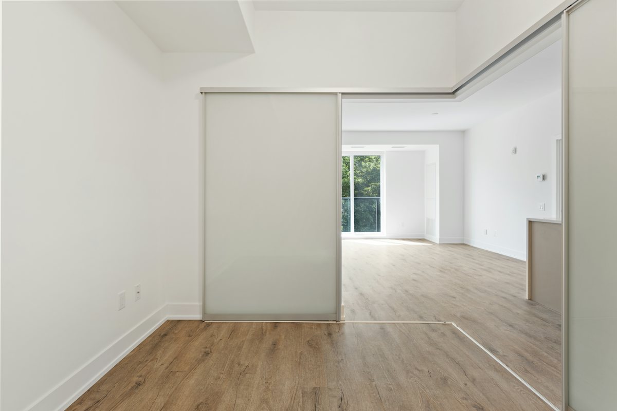 Empty bedroom with a large sliding closet door and light wood flooring.