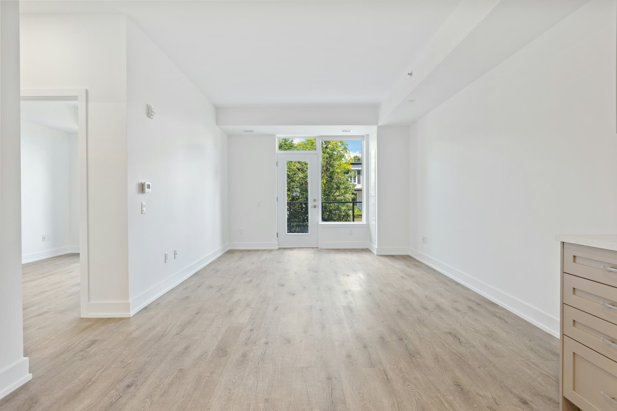 View from the bedroom doorway toward a window, with white walls and wood flooring.