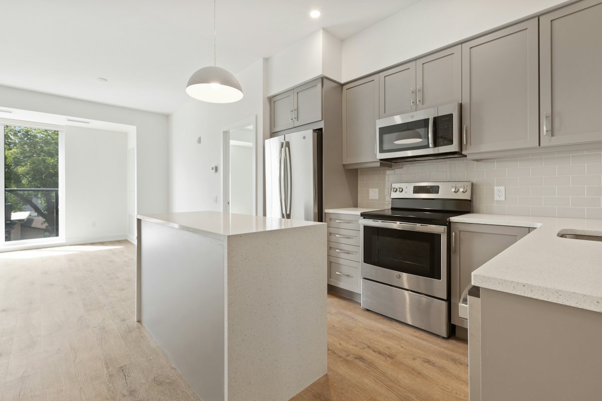 Empty kitchen with gray cabinets, stainless range and microwave, white island, and light wood flooring.