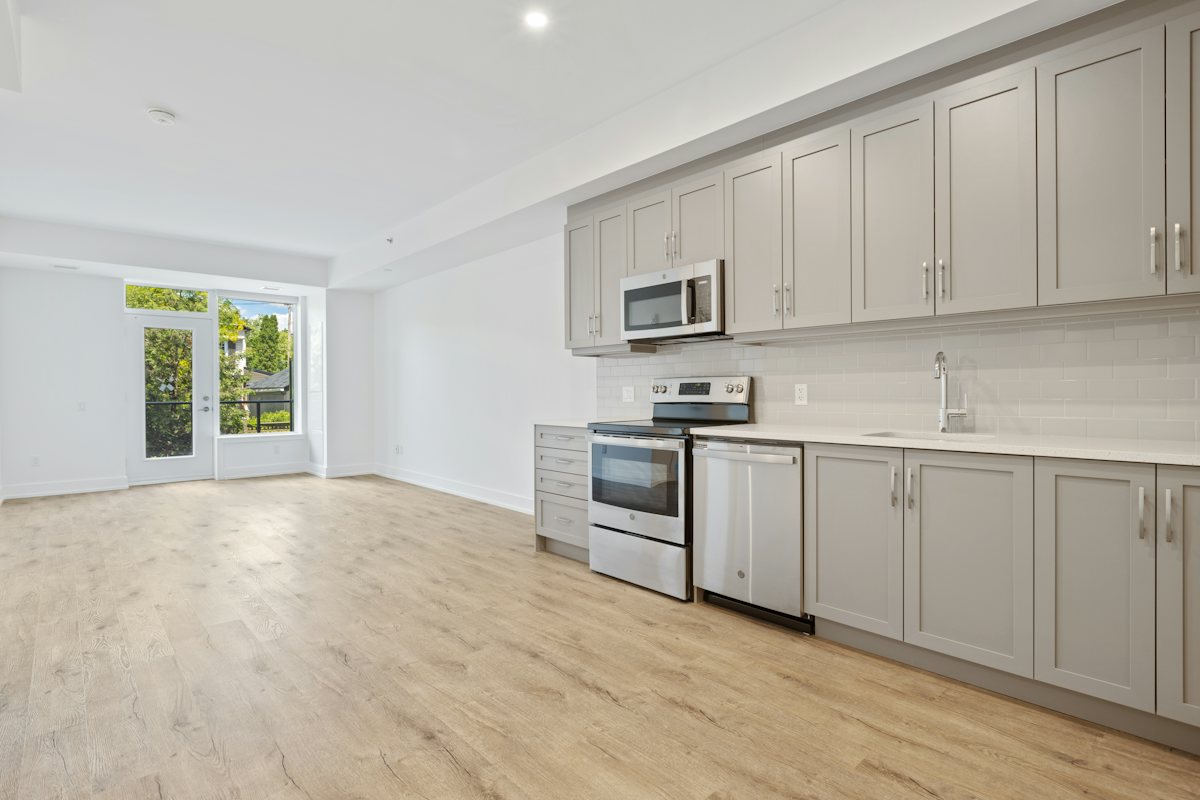 Kitchen wall of gray cabinets with range, microwave, and dishwasher, looking toward a glass door.